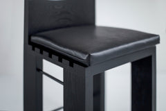Side profile of a black leather counter stool highlighting its metal frame