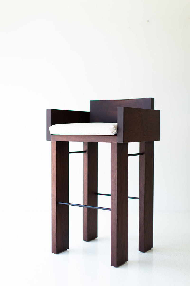 Full view of the organic modern Chile walnut bar stool with arms against a neutral backdrop