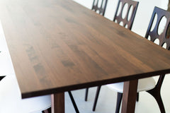 Modern walnut dining table with sculptural steel X-base, shown at an angle