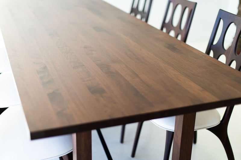 Modern walnut dining table with sculptural steel X-base, shown at an angle