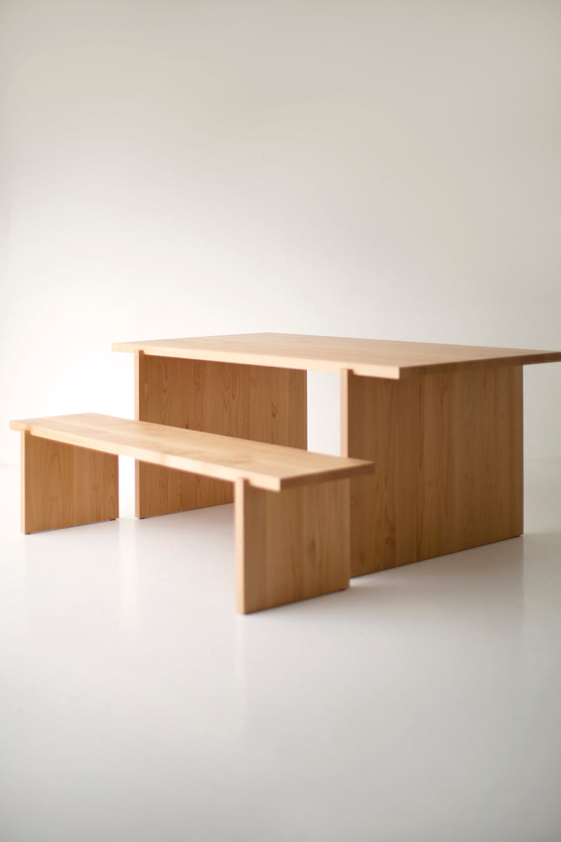 Angled view of a natural wood dining table paired with a matching bench