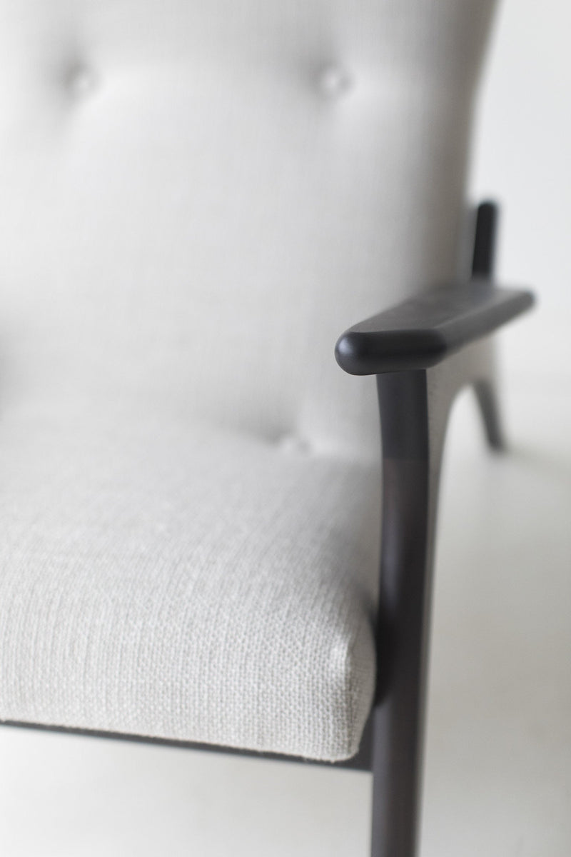 Close view of the sculpted dark walnut arm and grey upholstered seat