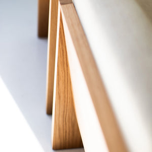 may include - modern luxury oak lounge chair with minimalist design, featuring clean lines and simple sleek shape. Chair sits in a clean white room with white floors. The overall aesthetic is modern. 08